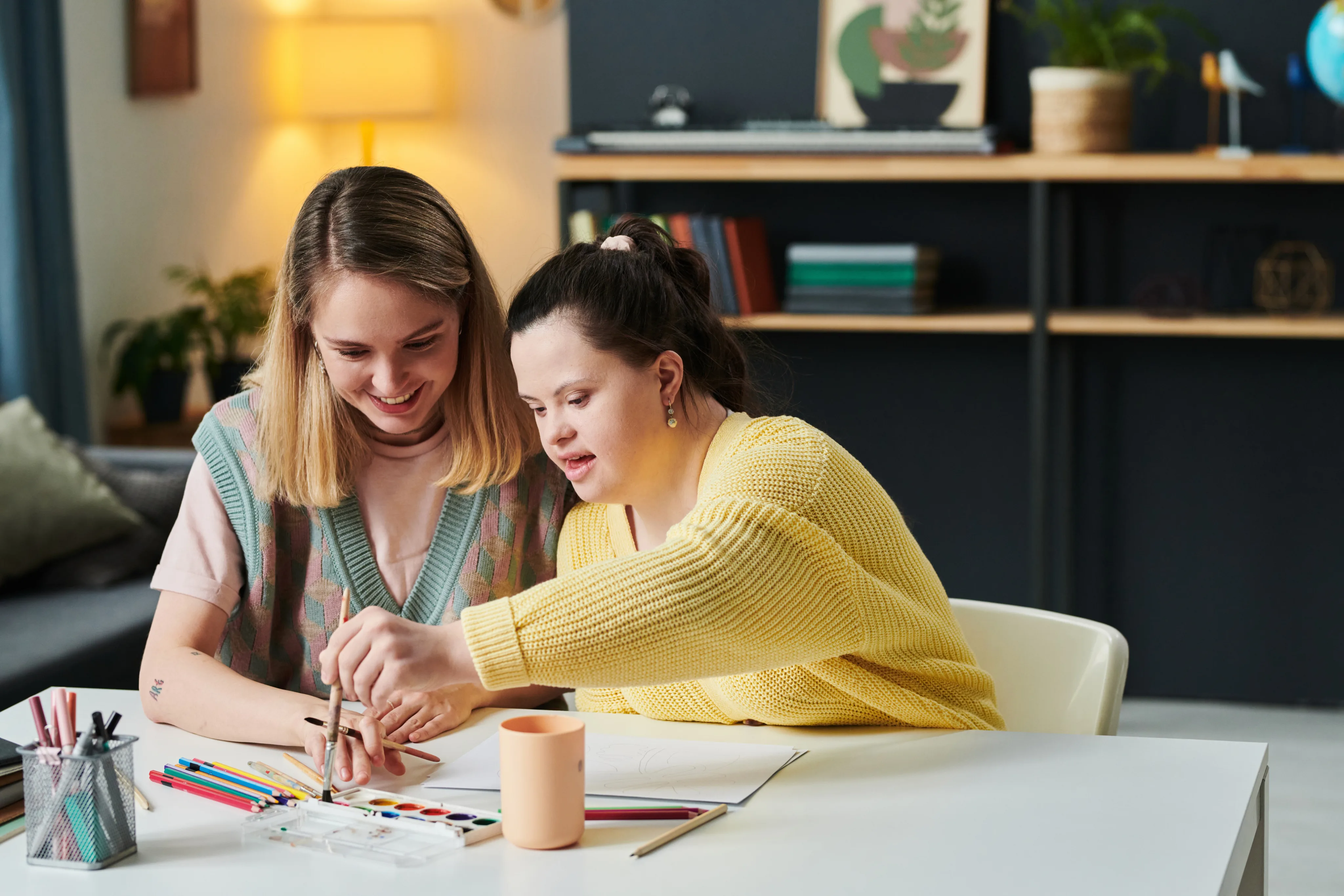 A support worker and an NDIS participant smiling while painting with watercolors together at a table.